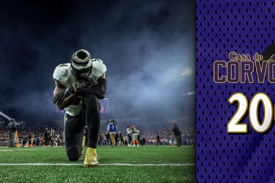 Homem de camisa branca ajoelhado em um gramado de estádio de futebol americano com o céu noturno, após derrota em partida de playoffs