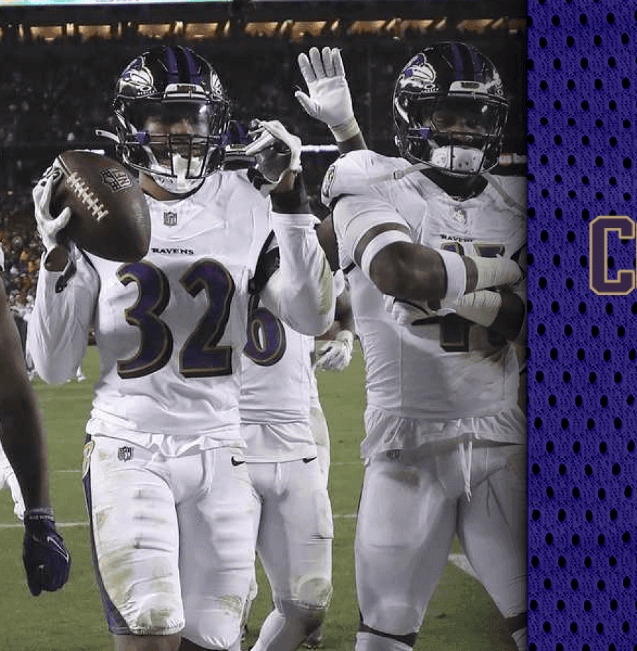Três jogadores de futbol americano trajando capacete preto, camisa e calças brancas com os adereços do Baltimore Ravens, com o jogador do meio segurando uma bola